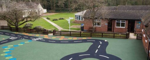 A wide lens shot of Meath school playground featuring astro turf and a pretend road for children to play on. A red brick classroom can be seen in the background.