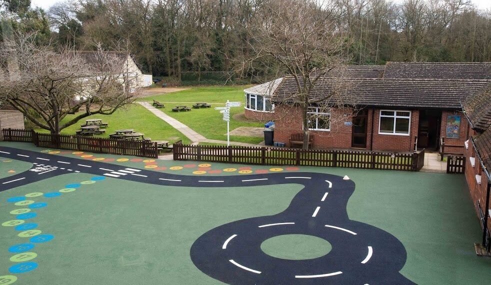 A wide lens shot of Meath school playground featuring astro turf and a pretend road for children to play on. A red brick classroom can be seen in the background.