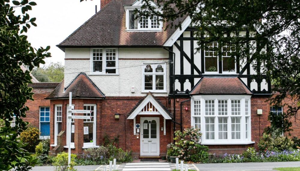 Meath School from the outside. It is a beautiful tudor style house with lots of windows. It features white paint and black accents.